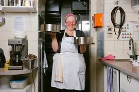 A Vollpension cook standing in a kitchen holding a tray