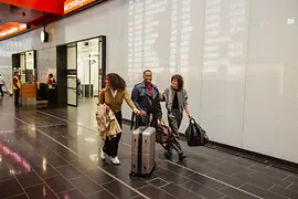 Drei Menschen mit Gepäck im Ankunftsbereich Flughafen Wien