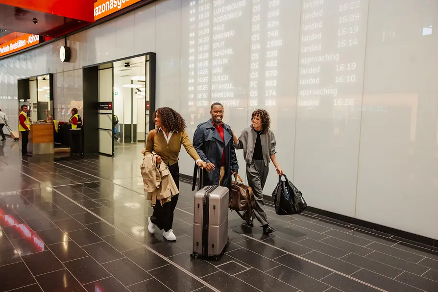 Three people with luggage in the arrivals area at Vienna Airport