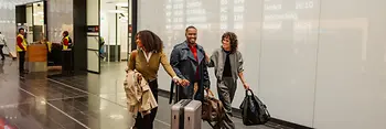 Drei Menschen mit Gepäck im Ankunftsbereich Flughafen Wien
