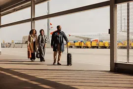 Menschen mit Handgepäck im Außenbereich des Flughafen Wien am Weg zum Terminal.